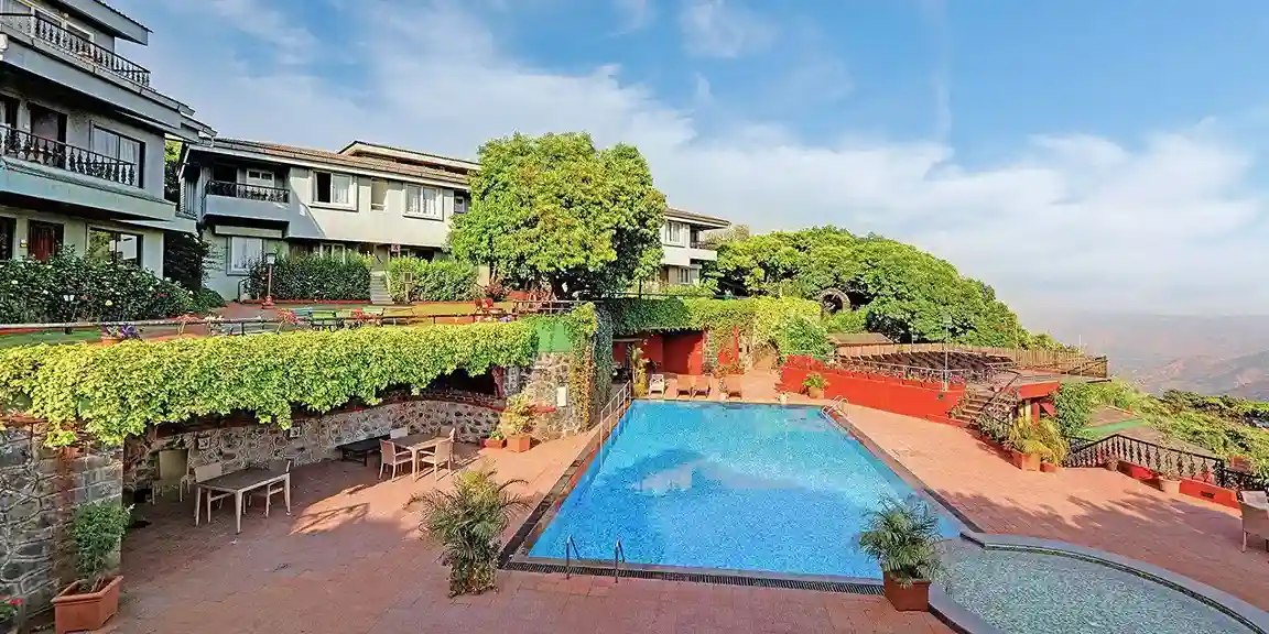 View of the swimming pool with resort buildings in the background at Ramsukh Resort.